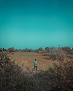 A friendly home inspector in a plaid shirt standing in a wide prairie field with rolling hills under a big blue sky.