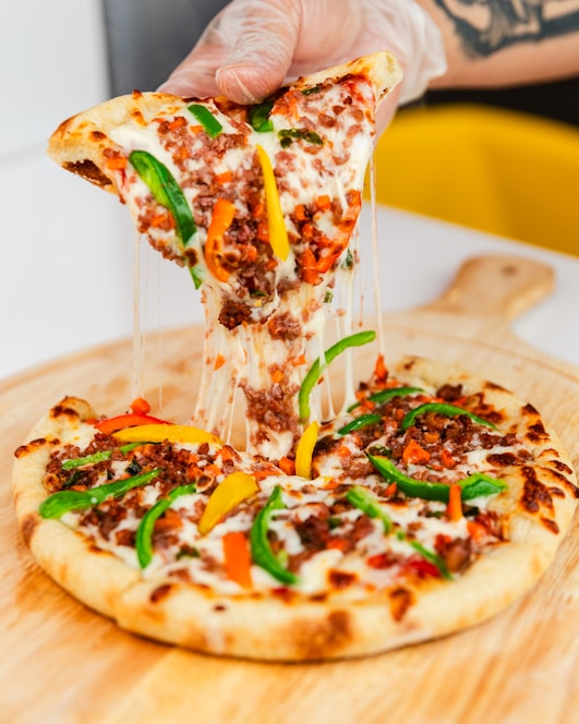 A close-up of a delicious, cheesy pizza slice being lifted from a wooden pizza board.