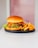 A delicious-looking chicken burger with crispy fried chicken, fresh lettuce, and sauce is placed on a round black plate. Next to the burger are golden-brown seasoned fries. The background is softly blurred, drawing attention to the food.