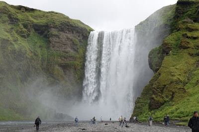 Tourists smiling and taking photos in front of a cascading waterfall.