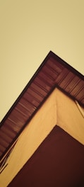 A perspective view of a building corner against a yellowish sky, with a focus on the roof's edge and siding.