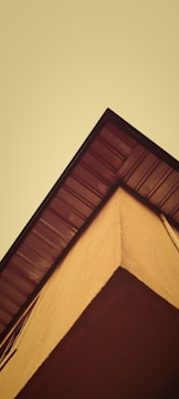 A perspective view of a building corner against a yellowish sky, with a focus on the roof's edge and siding.