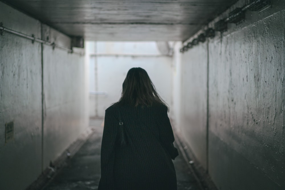 a woman walking down a long hallway in the dark