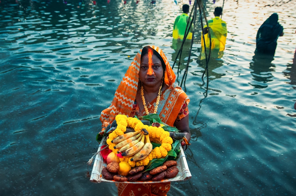 a woman standing in a body of water holding a tray of food
