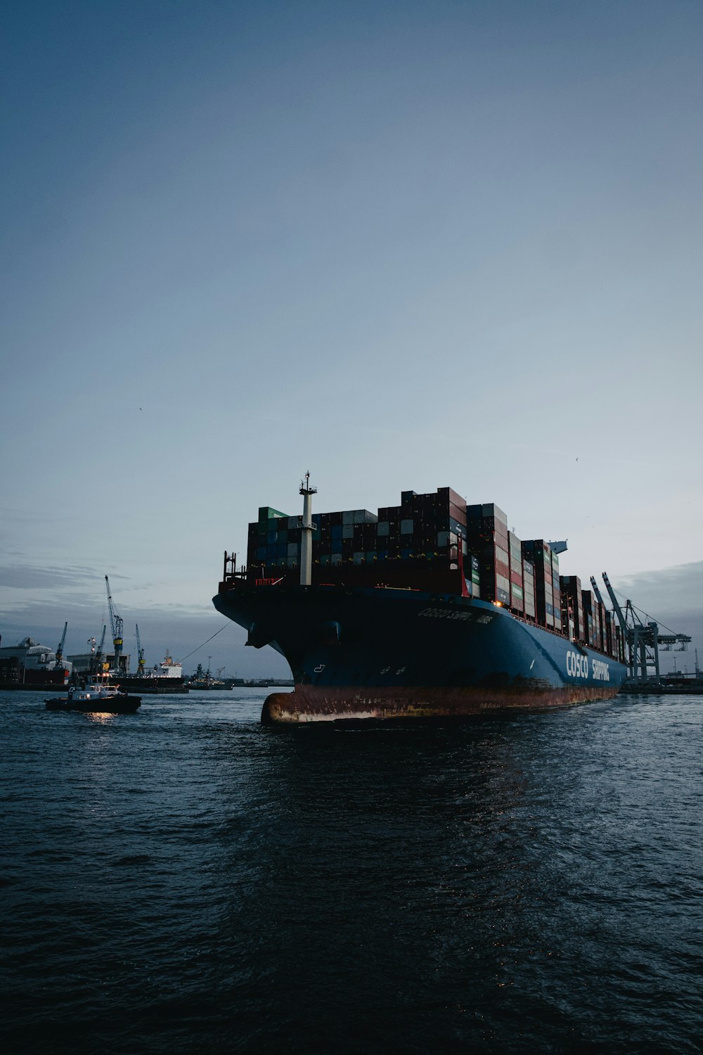 a large cargo ship in the ocean with a tug boat nearby