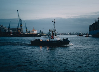 A tanker ship navigating through a busy port at sunset.