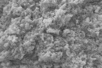 A close-up view of a textured surface resembling foam or porous material. The surface appears uneven with numerous small and large bubbles or holes throughout.