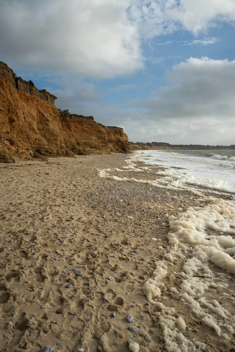 a sandy beach next to a cliff under a cloudy sky