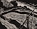 A monochromatic illustration featuring a dynamic composition with curved and sharp lines. It includes abstract forms that resemble a river or stream flowing past angular and curved structures, possibly rocks or hills, with a prominent object resembling a wooden bridge or structure.