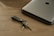 A sleek, minimalist keychain resting on a wooden desk next to a laptop.