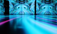 A large-scale digital art installation featuring swirling patterns of blue and cyan shades on a wall. The reflective surface in the foreground extends the patterns, creating a mesmerizing and immersive visual experience.