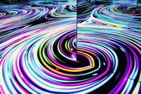 Vivid, swirling patterns of neon colors create a mesmerizing wave-like effect on a reflective surface. The movement is fluid and hypnotic, featuring loops and curves in an abstract form.