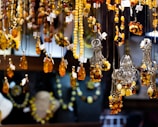 An array of amber jewelry, including necklaces and pendants, is displayed hanging in a showcase. The pieces are intricately designed with a range of warm amber tones, complemented by silver elements. Price tags are attached to each item, indicating they are for sale.