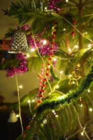 Festive decorations with green pine branches adorned with colorful ornaments, including shiny silver bells, red and pink beaded garlands, and bright string lights that create a warm, cheerful glow.