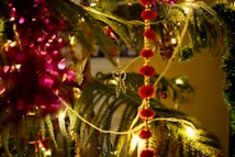 A close-up of Christmas decorations featuring evergreen branches adorned with colorful lights and red garlands. Glittering ornaments in gold and red accentuate the festive atmosphere.