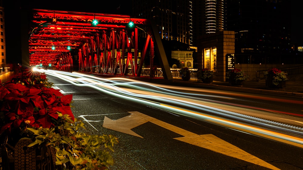 uma rua da cidade à noite com uma ponte vermelha ao fundo