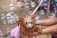 A small, long-haired dog is being held by a person, surrounded by colorful soap bubbles. The dog looks cheerful with its mouth open, and its fur is damp. The background appears to be sandy, suggesting an outdoor setting.