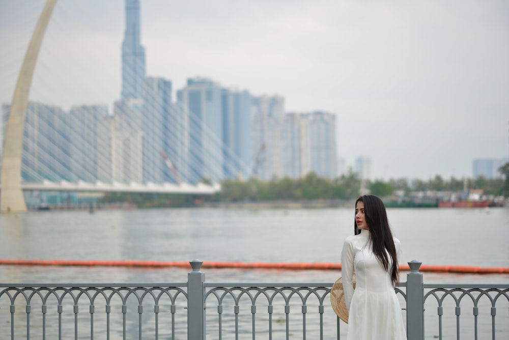 a woman in a white dress standing next to a fence