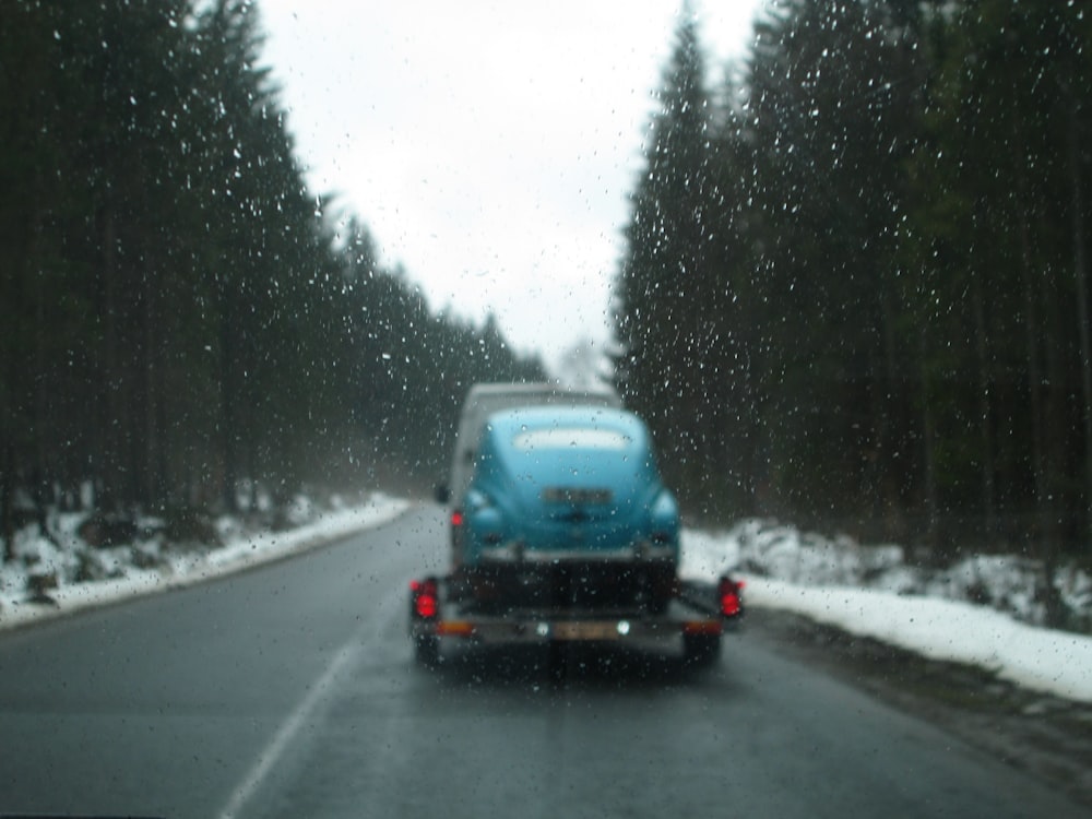 a blue truck driving down a snow covered road