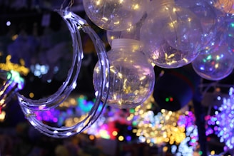 A cluster of glowing spherical light bulbs with delicate wire-like structures inside. A crescent moon-shaped decoration is wrapped in string lights, adding a dreamy ambiance. The background is filled with a vibrant array of colored lights, creating a festive atmosphere.