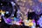 A cluster of glowing spherical light bulbs with delicate wire-like structures inside. A crescent moon-shaped decoration is wrapped in string lights, adding a dreamy ambiance. The background is filled with a vibrant array of colored lights, creating a festive atmosphere.