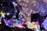 A cluster of glowing spherical light bulbs with delicate wire-like structures inside. A crescent moon-shaped decoration is wrapped in string lights, adding a dreamy ambiance. The background is filled with a vibrant array of colored lights, creating a festive atmosphere.