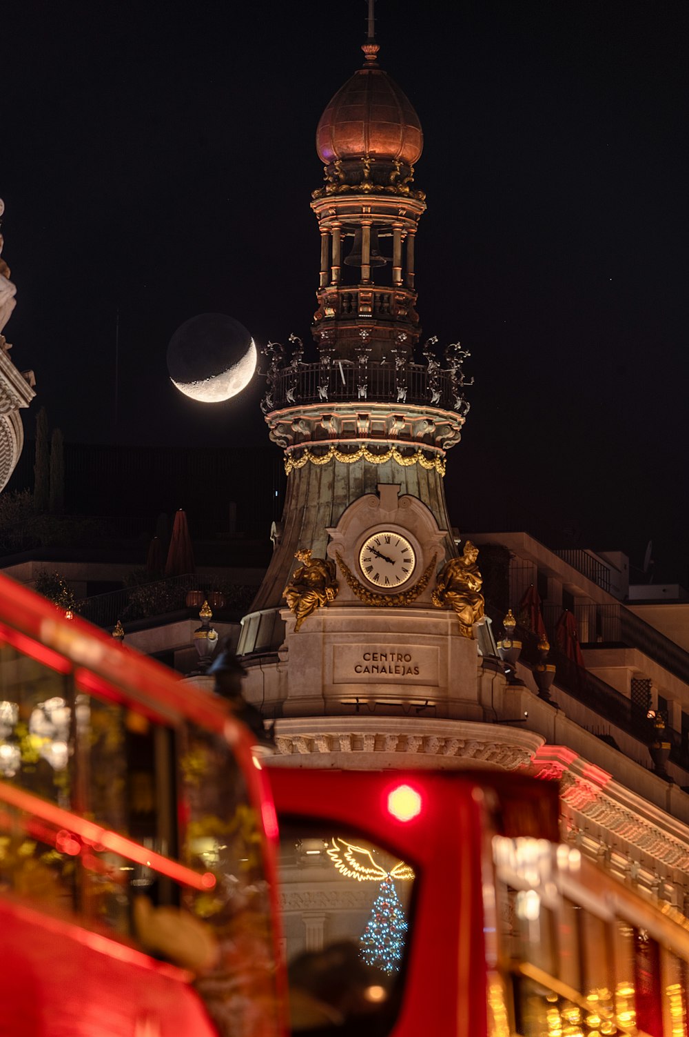 a red double decker bus driving past a clock tower