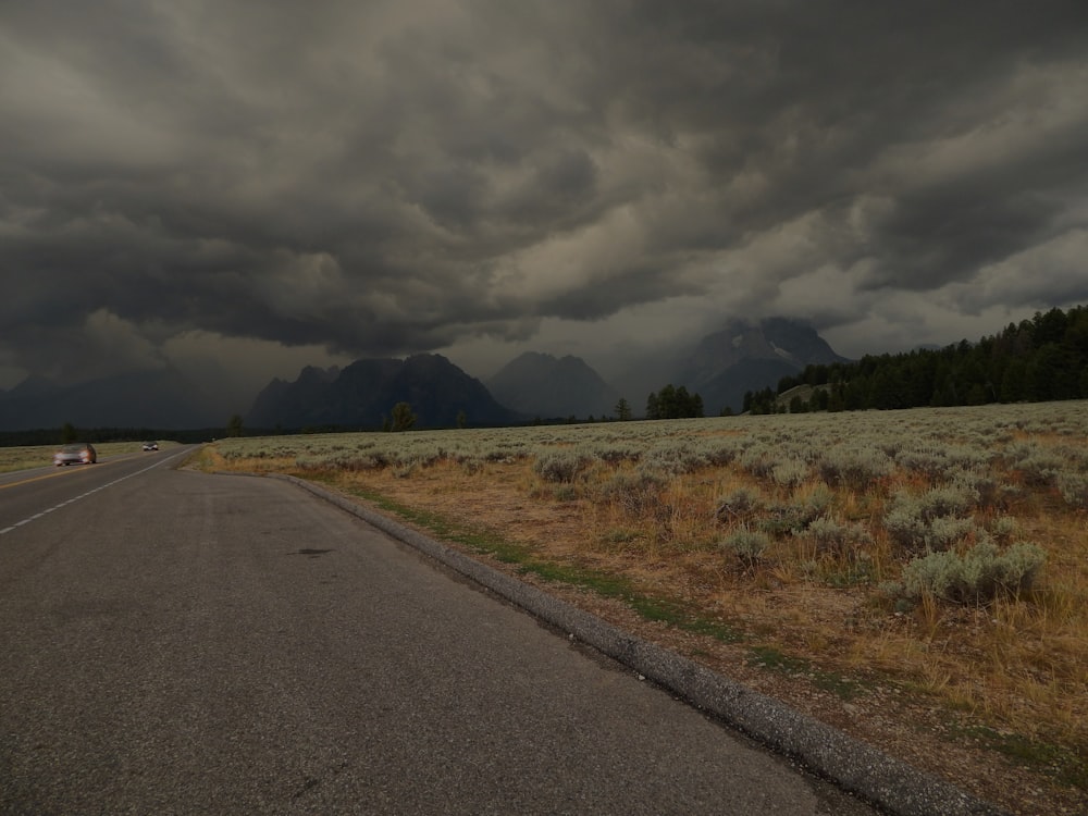 a road in the middle of a field with mountains in the background