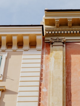 A detailed close-up of classic architectural elements featuring ornate cornices and decorative moldings. The structure showcases a blend of smooth and textured surfaces with intricate detailing around the edges.