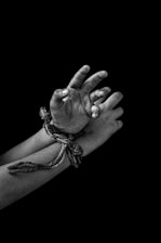 A pair of hands bound together with a rope, positioned against a dark background. The hands appear to be dirty or smudged, emphasizing a sense of struggle or distress.