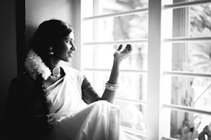 A serene moment of a girl wearing a classic South Indian half-saree, standing by a window with natural light.