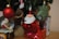 A Christmas-themed scene features various decorations including a red spherical ornament with a Santa face, a glittery green star ornament, a candy cane with red and white stripes, and a Santa figurine inside a snow globe. Burlap and wrapped gifts add to the festive atmosphere.