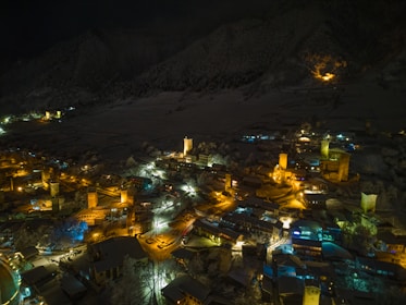 A panoramic view of a Minecraft village illuminated by glowing lanterns and mystical shaders at night.
