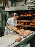 Baker pulling freshly baked bread out of the oven in a rustic bakery setting.