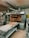A commercial bakery setup featuring a large industrial oven with several racks of freshly baked bread. The oven has trays inside with bread visible through the open doors. There is also a conveyor belt in front with additional loaves placed on it.