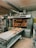 A commercial bakery setup featuring a large industrial oven with several racks of freshly baked bread. The oven has trays inside with bread visible through the open doors. There is also a conveyor belt in front with additional loaves placed on it.