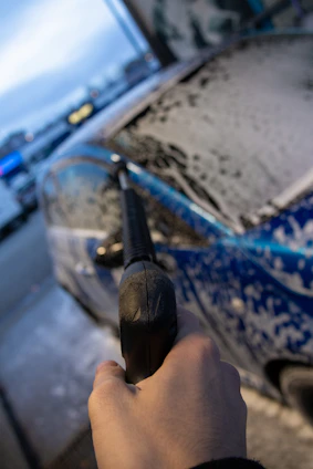 A sleek pressure washing machine spraying water over a dark driveway with reflective wet surfaces under a soft blue sky.