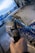 A close-up view of a person holding a pressure washer wand, spraying soapy water onto a car. The vehicle is covered in a layer of foam, and the scene takes place outdoors, possibly at an automatic car wash facility.
