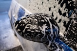 Foamy hand wash in progress, bubbles glistening on a luxury sedan’s surface.