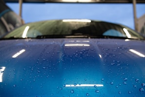 Close-up of a sleek black car hood glistening with water droplets under electric blue lighting.