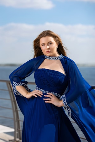 Model wearing a flowing navy blue dress with asymmetrical hem, standing on an urban rooftop.