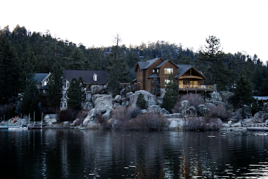 A cozy lakeside home nestled among tall pine trees with a serene lake reflecting the sunset.