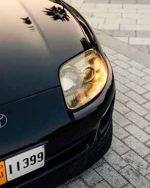 Close-up of a sleek black luxury car's glossy hood reflecting soft ambient light.