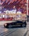 A sleek black sports car is parked in front of an illuminated arena entrance, with a large sign bearing the name of a famous beverage brand. The building features a modern, geometric facade with bright red and blue lights, creating a vibrant and lively atmosphere.