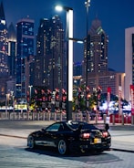 A sleek black sports car with a glossy custom wrap reflecting city lights at dusk.