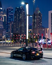 A sleek black car parked outside a bustling city skyline at dusk.