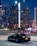 A sleek luxury car parked in an upscale urban setting with vibrant city lights.