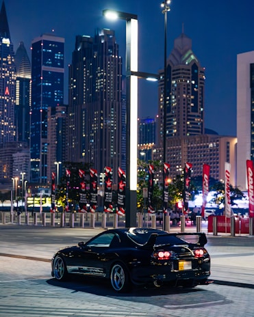 A vibrant cityscape at night with a sleek sports car parked on the street.