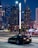 A sleek luxury car parked in an upscale urban setting with vibrant city lights.
