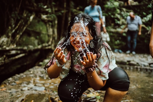 A smiling person gently cleansing their face with water splashing softly.